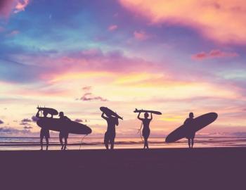 friends carrying surfboards on the beach at sunset
