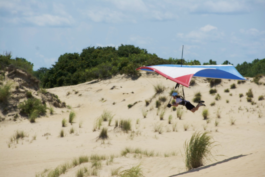 A hang gliding pilot flies over shrubs and grasses at the base of Jockey's Ridge. A hang gliding pilot flies over shrubs and grasses at the base of Jockey's Ridge.